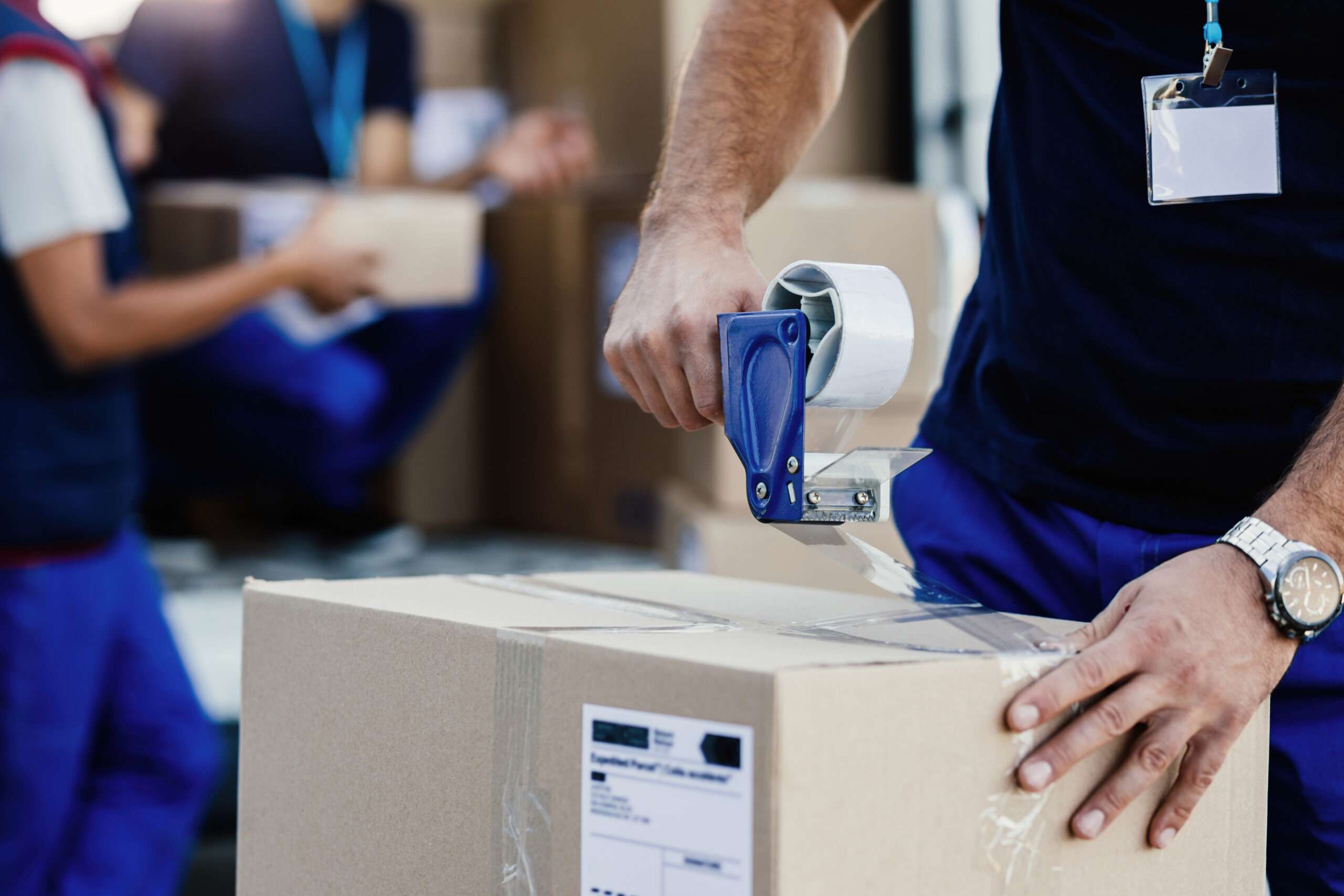 close up of worker using tape dispenser while packing cardboard